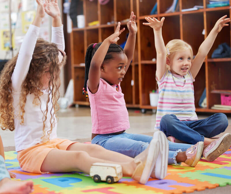 Three young girls reaching up with arms
