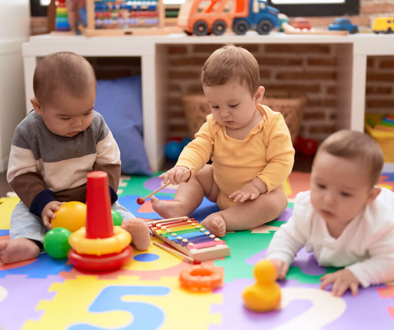 Three babies sitting and interacting with educational toys