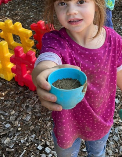 A young girl holding up a cup of dirt