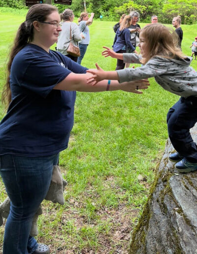 A young girl standing on a rock reaching out to a wome to catch her